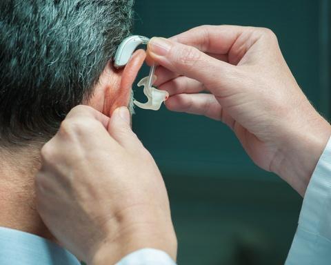 Physician places hearing aid over a man's ear