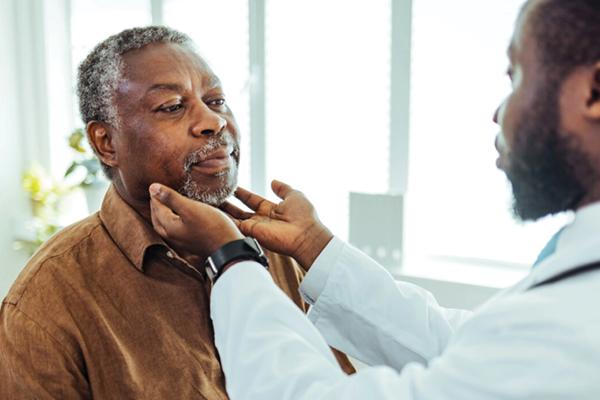 A male patinet being examined by a provider whose hands are on patient's neck