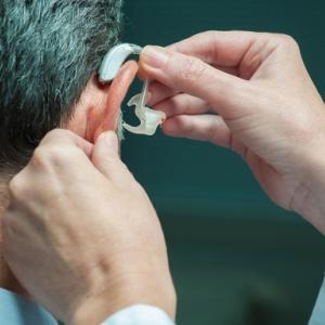 Physician places hearing aid over a man's ear