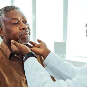 A male patinet being examined by a provider whose hands are on patient's neck