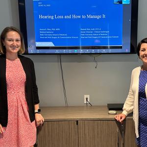 Dr. West and Dr. Hannah Heet in front of their presentation slides 